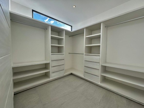 House for sale on Huayacan Ave – Modern dressing room with built-in light-wood closets, lit by a high horizontal window