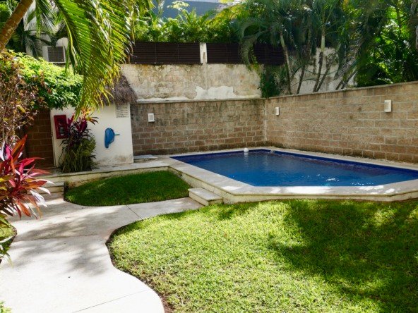 Departamento en venta en centro cancún - alberca rectangular en patio trasero rodeado de un jardín tropical y un muro de piedra